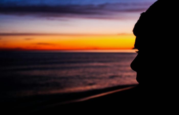 Silhouette of a woman meditating at sunrise with vibrant pink sky.
